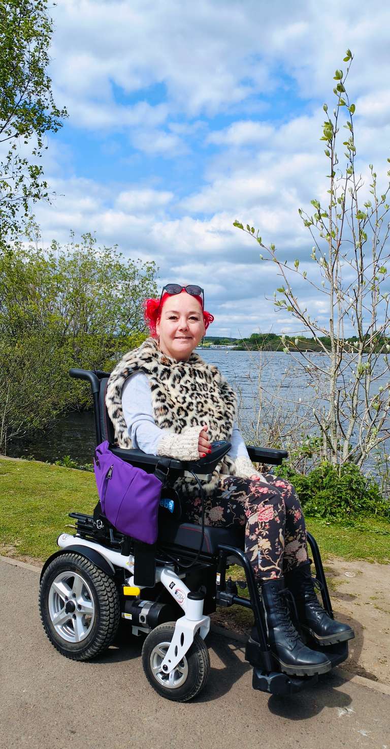 Me in my powered wheelchair by Chasewater lake, dressed in my trademark leopard print coat and light blue jumper. My wheelchair's looking smart with its purple bag attachment, and I've got my red nails and hair to match! Perfect spot for some wheelchair adventuring with a gorgeous view of the water. Who needs walking when you've got wheels with this much style?