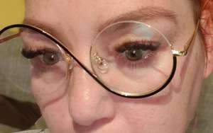 Close-up selfie of a woman with auburn hair wearing large round gold-rimmed glasses, showing off freshly done eyelash extensions and shaped eyebrows