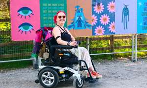 Me absolutely buzzing in my wheels at what looks like a proper festival spot! Rocking my festival gear, sunnies on, with the most incredible colourful street art behind me - eyes, flowers, and all sorts of gorgeous murals. This is exactly what Wheely Happy Days is about - getting out there, soaking up the good vibes, and showing that wheels don't stop the adventure! 🌈✨
