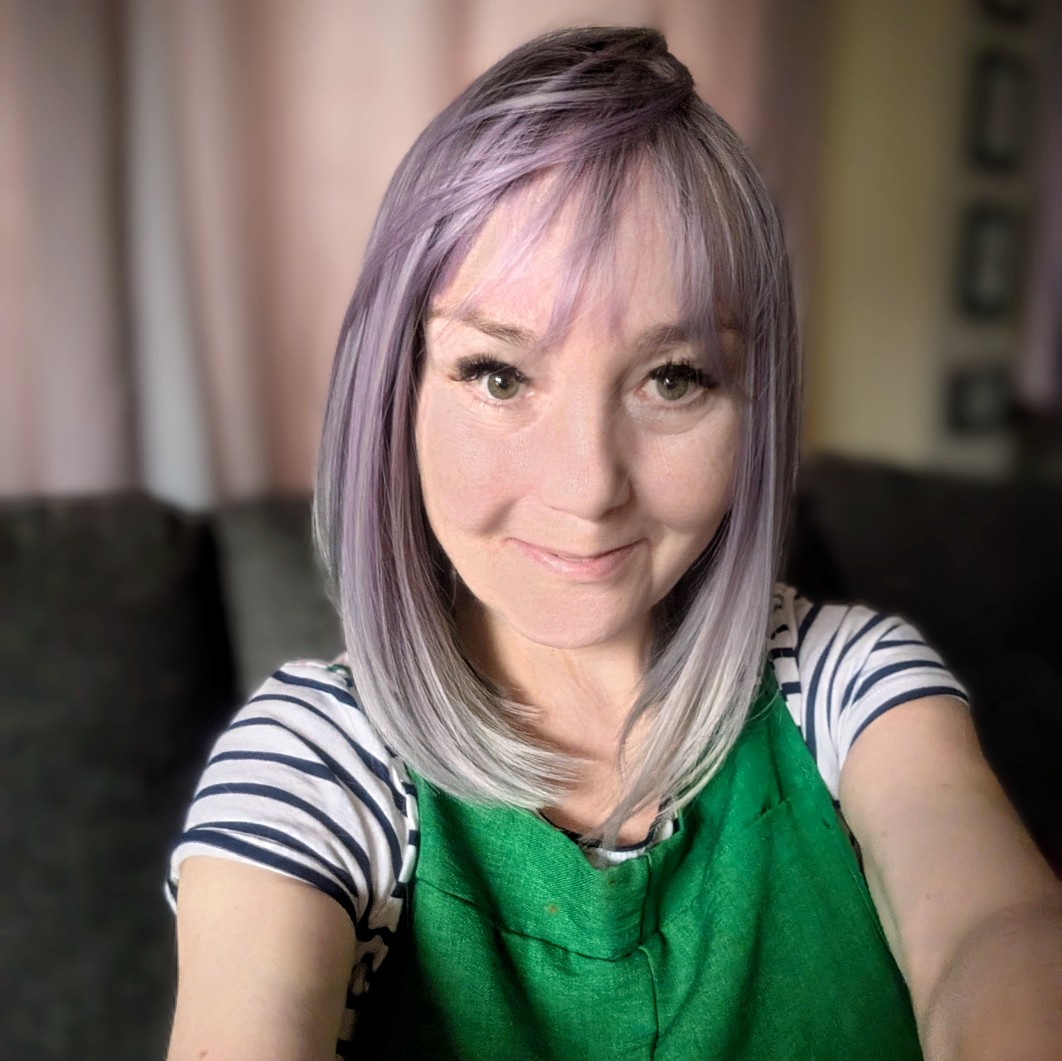 Sha's happy Sunday selfie — lavender and silver ombre bob wig with a pink-toned fringe, green dungarees over a stripy top, and a smile that says "today was a good day actually." 💜