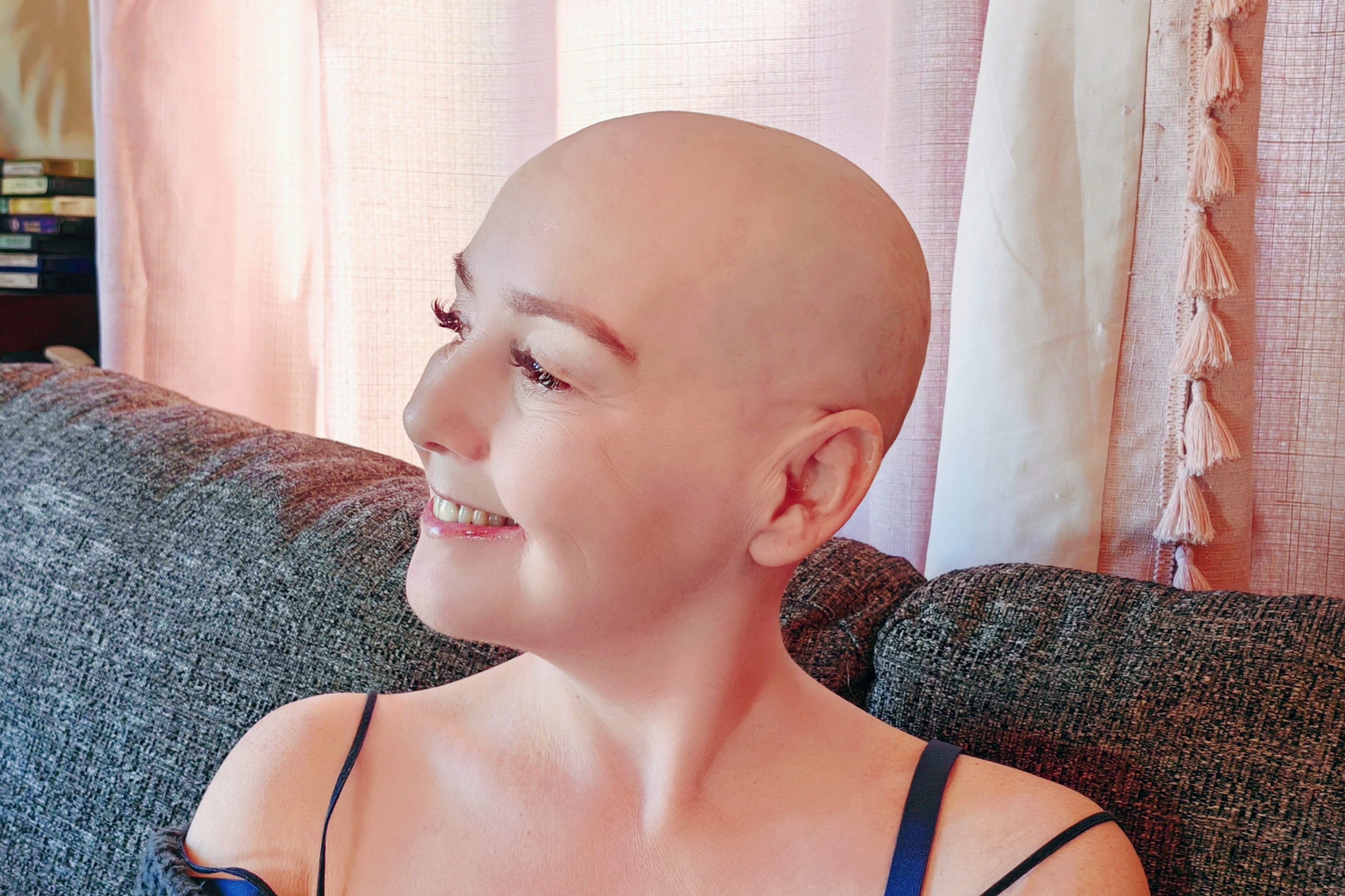 A side profile shot of Sha, head freshly shaved, laughing and looking off to one side. The soft light from the window catches her face beautifully. She looks relaxed, confident, and genuinely happy — someone who made a decision on her own terms and is entirely at peace with it. 💜